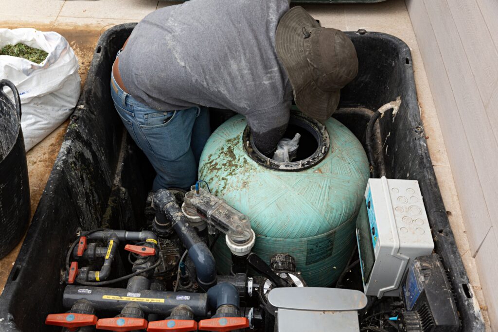 Personne retirant le sable d’un filtre à sable de piscine pour le remplacer
